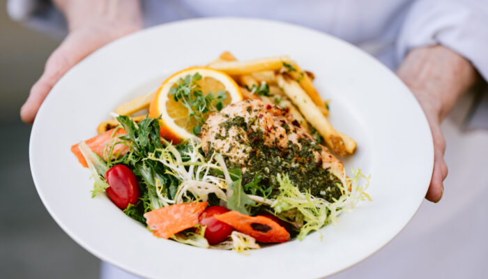 Person holds plate with greens, meat and fries